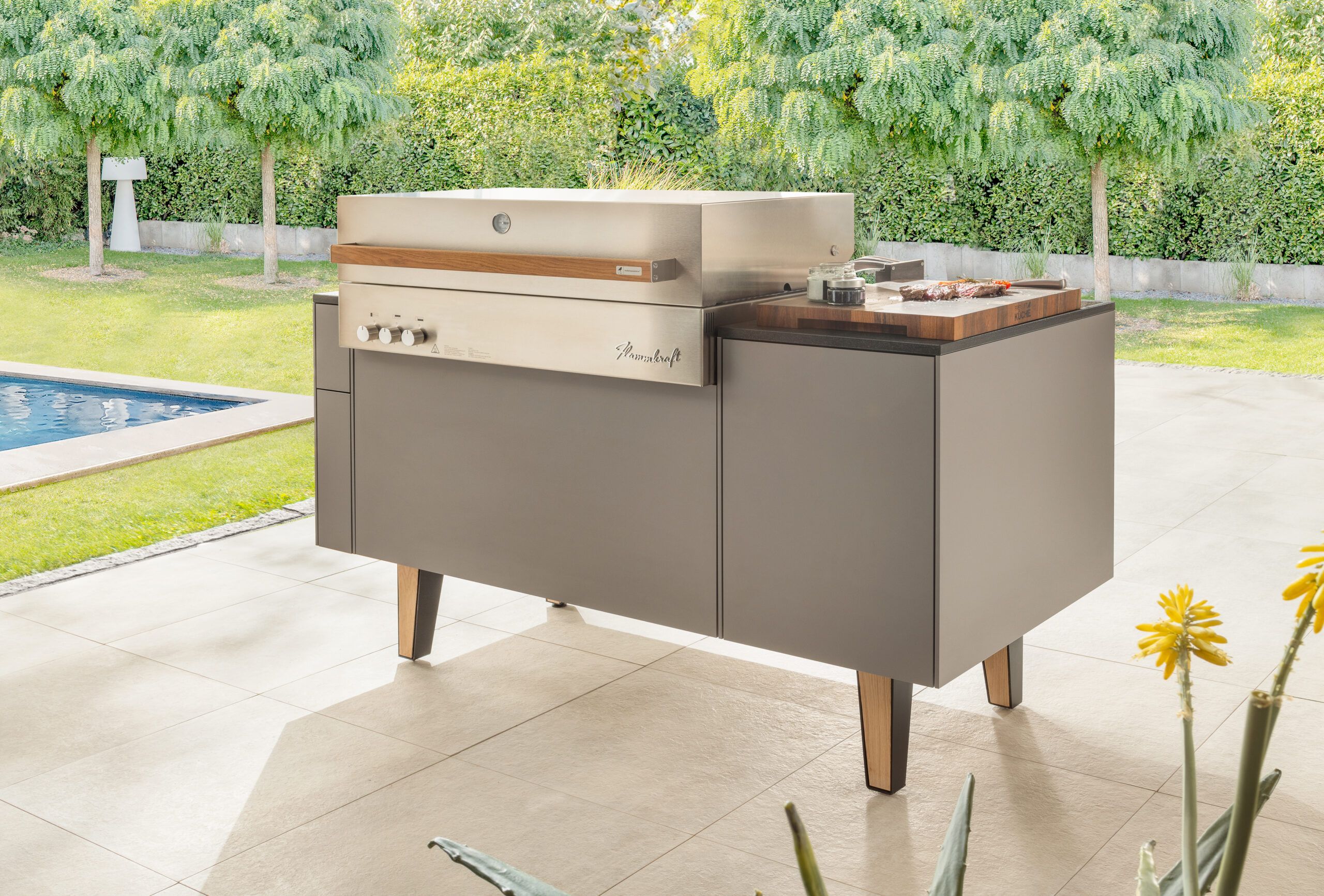 Graue Freiluftmanufaktur Freiluftinsel mit Flammkraft Gasgrill in einem Garten