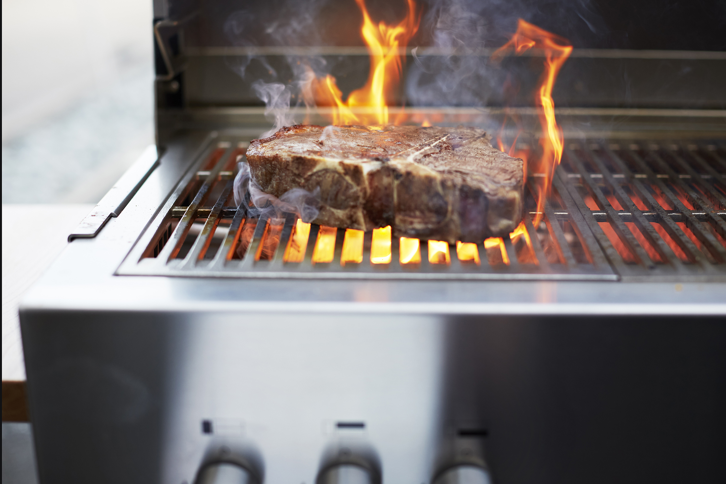 Perfektes Branding und maximale Hitze: Saftiges Fleisch wird auf einem Flammkraft Premium-Grill scharf angebraten. Die Nahaufnahme zeigt professionelles Outdoor-Cooking auf einer Terrasse.